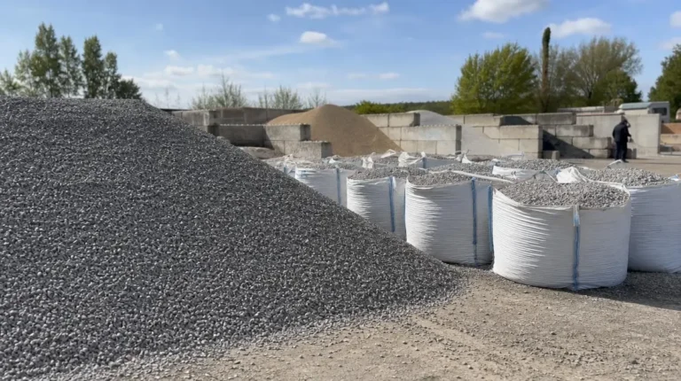 Tas de gravier gris au premier plan et big bags blancs remplis de gravier alignés sur une plateforme de stockage de matériaux